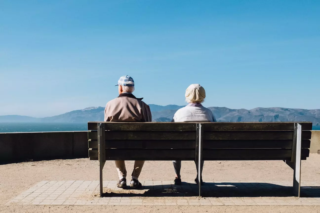 elederly couple sitting on a bench overlooking a scenic landscape
